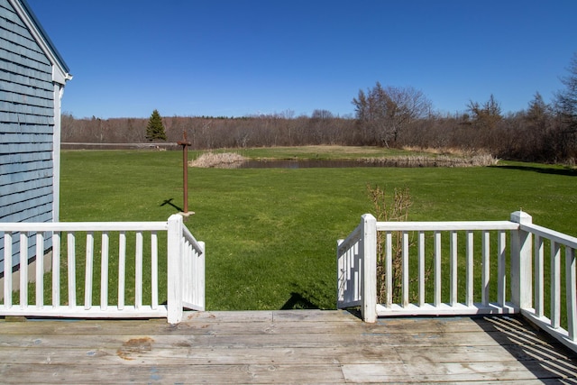 view of green lawn with a deck with water view