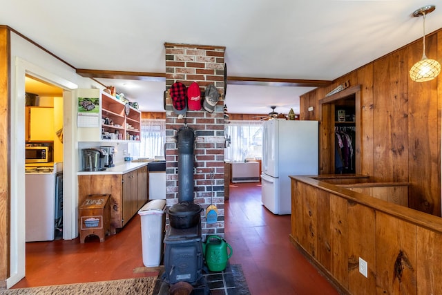 kitchen featuring freestanding refrigerator, a wood stove, stainless steel microwave, brown cabinetry, and wooden walls