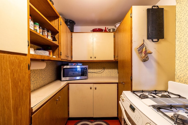 kitchen featuring stainless steel microwave, white gas range oven, light countertops, and open shelves