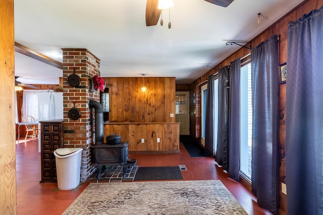 living room featuring ceiling fan, wood walls, a wood stove, and wood finished floors