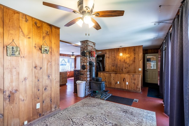 living area featuring wood walls, ceiling fan, and a wood stove