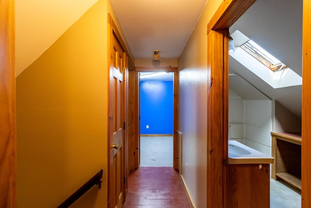 corridor featuring a skylight, wood finished floors, and baseboards