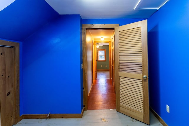 hallway with baseboards, vaulted ceiling, and wood finished floors