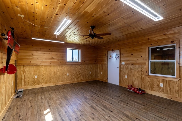 empty room featuring wood finished floors, wood walls, wood ceiling, baseboards, and a ceiling fan