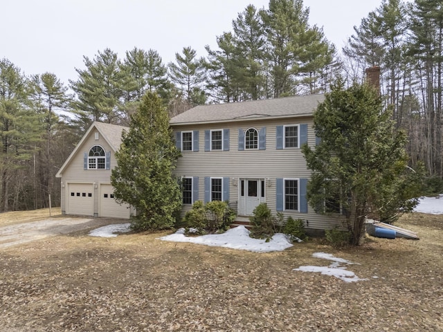 colonial-style house featuring a chimney, driveway, and a garage