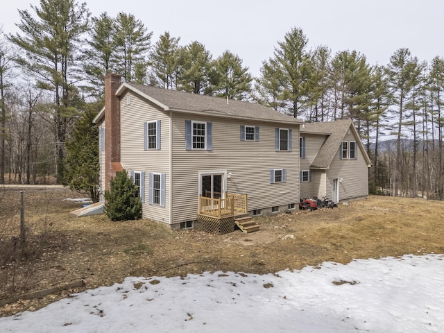 snow covered property with a chimney, a wooden deck, and roof with shingles
