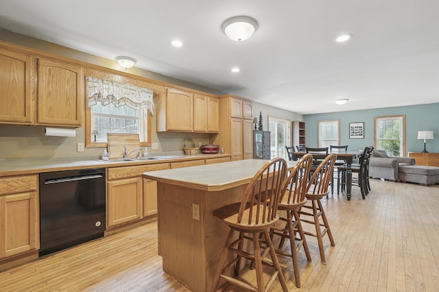 kitchen featuring light wood-type flooring, light countertops, a breakfast bar, and black dishwasher