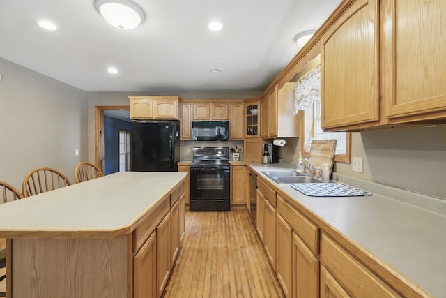 kitchen with a breakfast bar, light countertops, a sink, black appliances, and light wood-style flooring