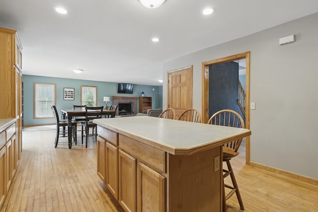 kitchen featuring light countertops, a center island, light wood-style flooring, a brick fireplace, and a breakfast bar area
