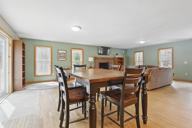 dining room featuring a fireplace, light wood finished floors, and baseboards