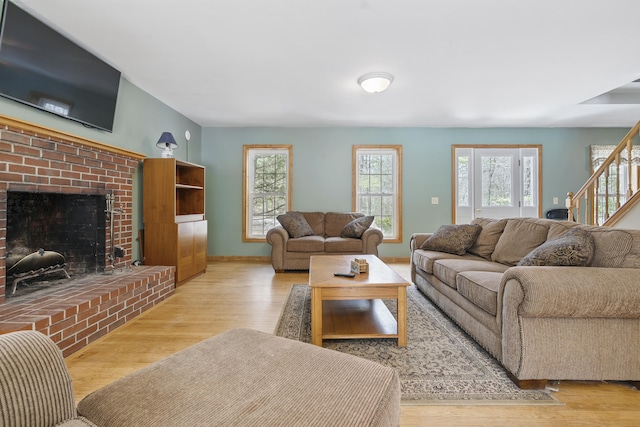 living room featuring wood finished floors, a brick fireplace, baseboards, and stairway