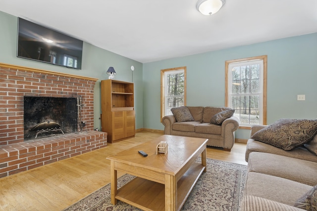 living room featuring baseboards, a brick fireplace, and wood finished floors