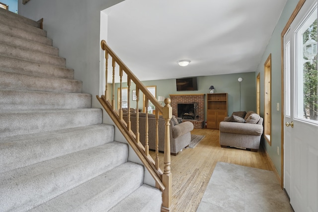 staircase with a brick fireplace and wood finished floors