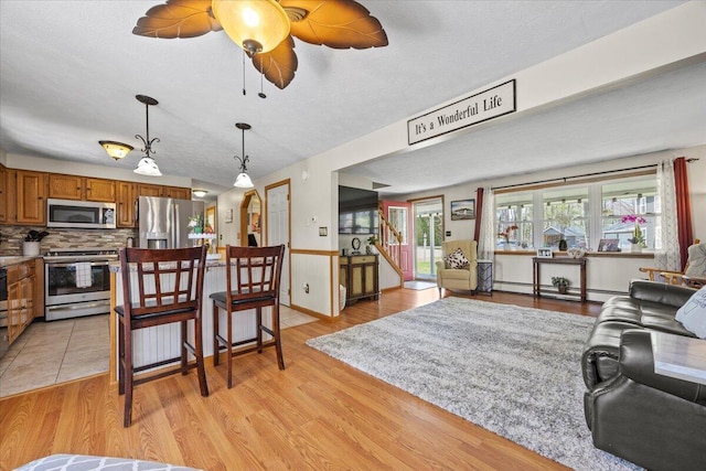 living room with a baseboard heating unit, a ceiling fan, and light wood finished floors