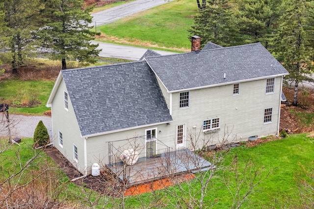 back of house featuring a yard, a wooden deck, a shingled roof, and a chimney