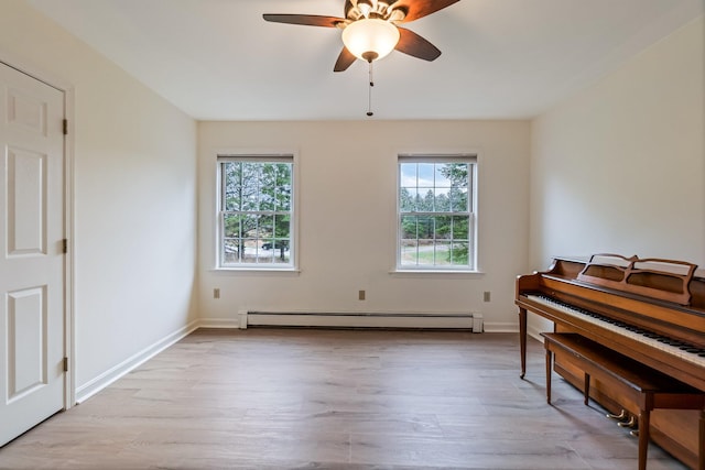 living area with ceiling fan, a wealth of natural light, light wood-type flooring, and a baseboard heating unit
