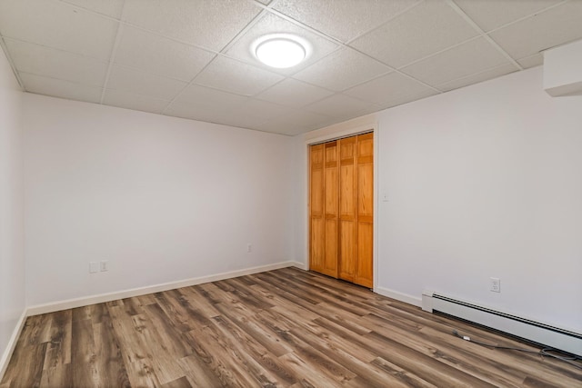 interior space featuring a paneled ceiling, a baseboard radiator, baseboards, and wood finished floors