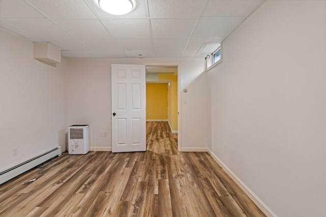 below grade area featuring a baseboard radiator, wood finished floors, baseboards, and a drop ceiling
