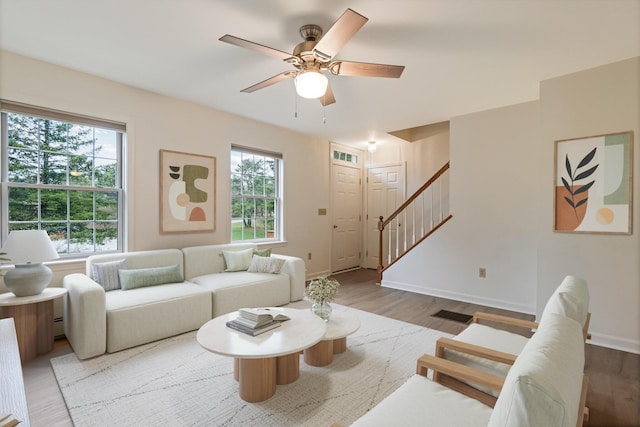 living area featuring baseboards, wood finished floors, a ceiling fan, and stairs