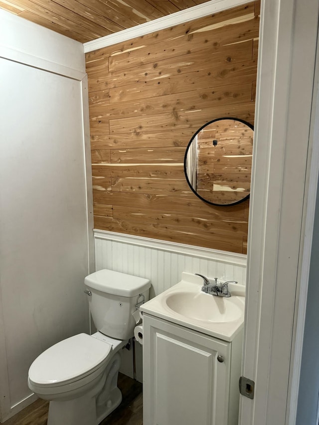 half bath with wooden walls, vanity, toilet, and wood ceiling