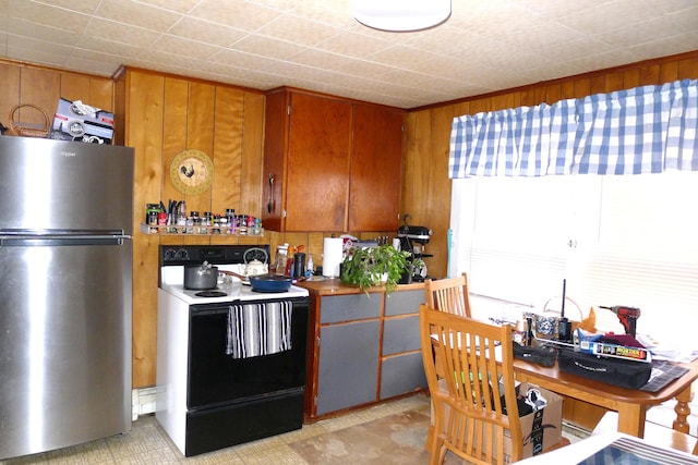 kitchen featuring range with electric stovetop, wooden walls, freestanding refrigerator, and brown cabinets