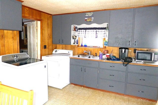 kitchen with a sink, stainless steel microwave, washing machine and dryer, gray cabinetry, and wood walls