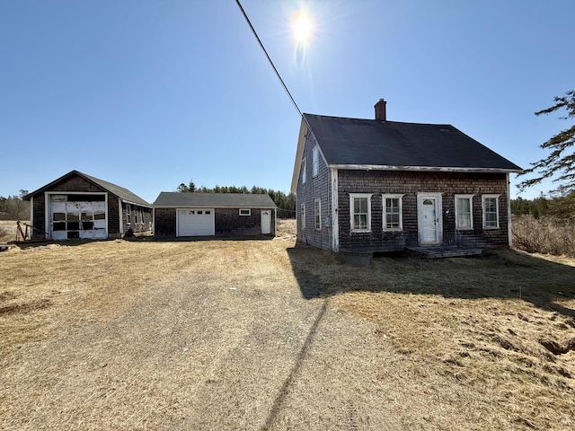 view of side of home with a garage, an outbuilding, a chimney, and driveway