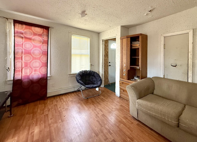 living room with baseboard heating, a textured wall, wood finished floors, and a textured ceiling