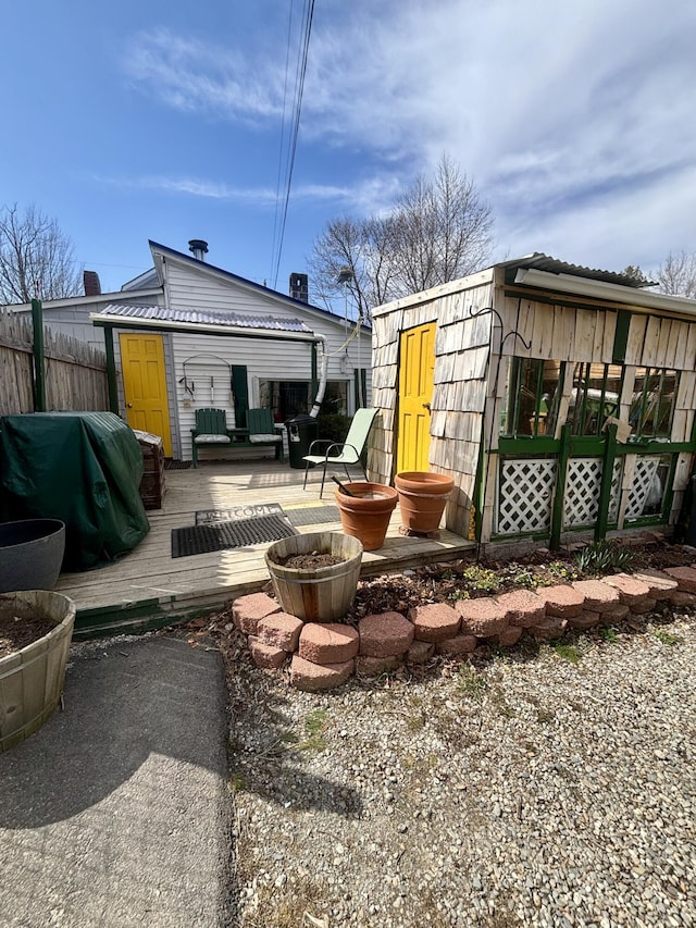 back of property with fence, an outbuilding, and a deck