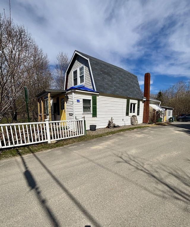 view of home's exterior with fence, covered porch, a shingled roof, and a gambrel roof