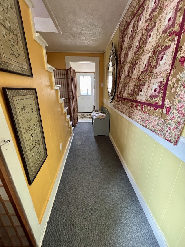 hall with ornamental molding, dark colored carpet, stairs, and a textured ceiling