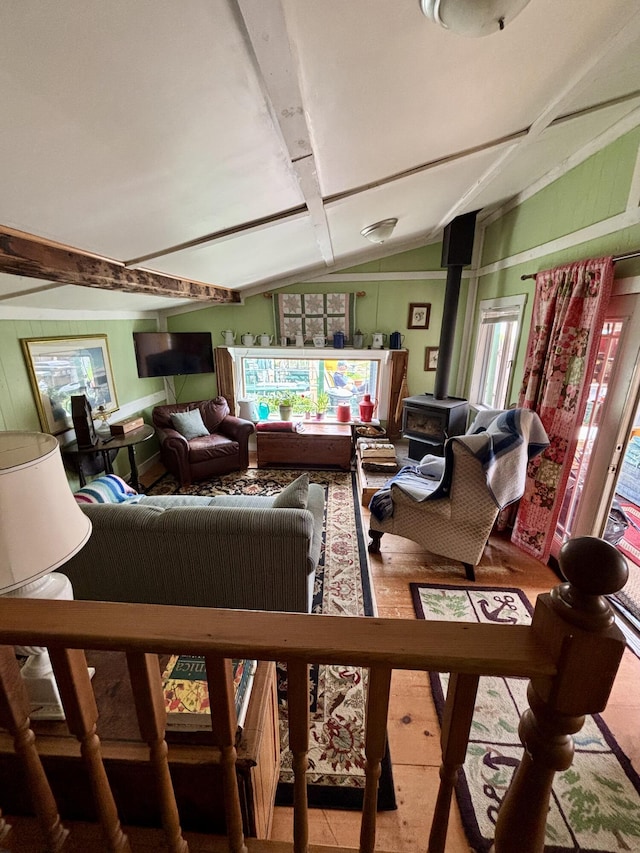 living room with wood walls, lofted ceiling with beams, a wealth of natural light, and a wood stove