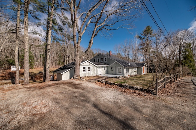 view of front facade with a chimney, an outdoor structure, fence, dirt driveway, and a shed