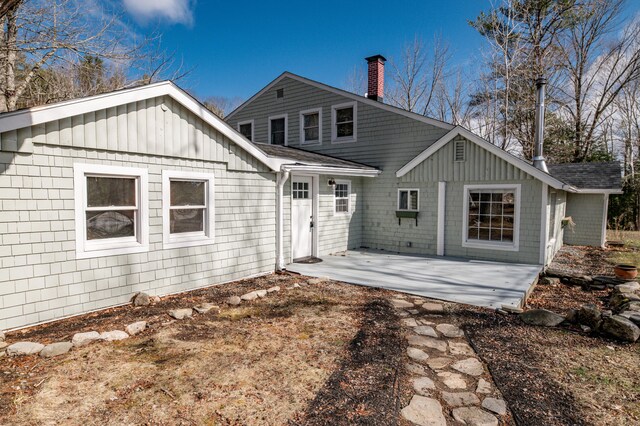 back of house with roof with shingles, a chimney, a patio area, and board and batten siding
