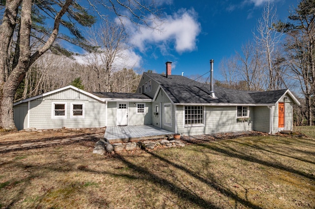 rear view of house featuring a lawn, roof with shingles, a chimney, and a wooden deck