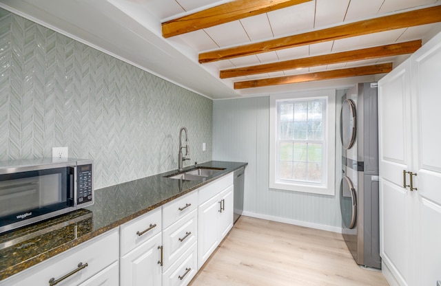 washroom featuring a sink, stacked washer / drying machine, light wood-style floors, baseboards, and laundry area