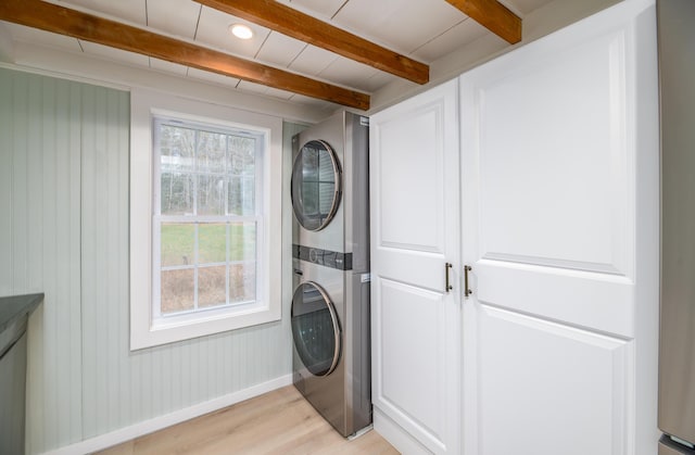 laundry room featuring baseboards, stacked washer and clothes dryer, and light wood-style floors
