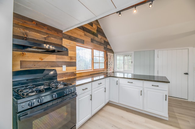 kitchen featuring black range with gas stovetop, light wood-style floors, wooden walls, white cabinets, and lofted ceiling