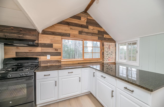 kitchen with dark stone countertops, white cabinetry, wood walls, vaulted ceiling, and black range with gas cooktop