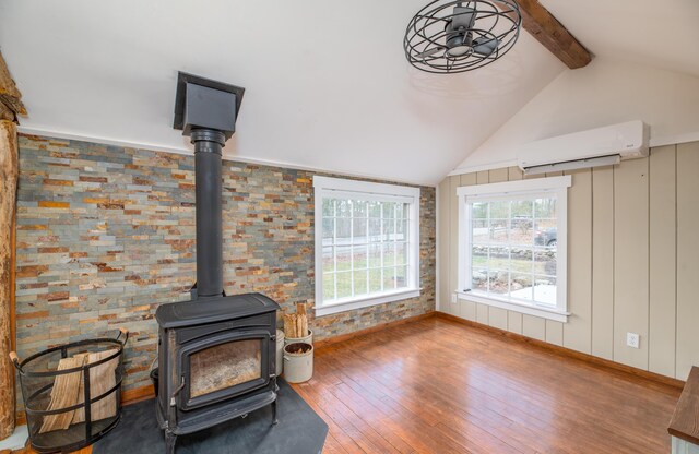 unfurnished living room featuring vaulted ceiling with beams, a wall mounted air conditioner, a wood stove, and wood-type flooring