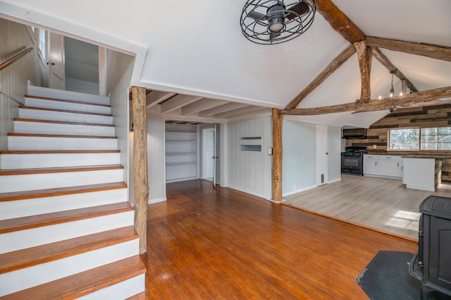 unfurnished living room with stairway, wood finished floors, wood walls, and lofted ceiling with beams