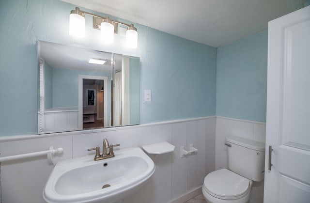 full bathroom with toilet, wainscoting, and a sink