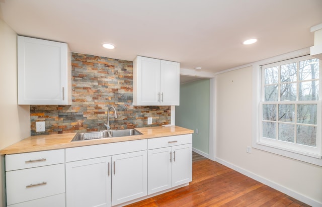 kitchen featuring tasteful backsplash, white cabinets, a sink, baseboards, and light wood-type flooring