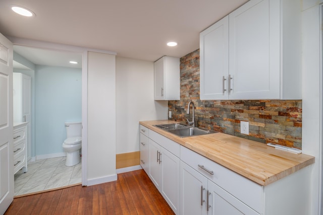 kitchen featuring a sink, decorative backsplash, baseboards, hardwood / wood-style floors, and white cabinets