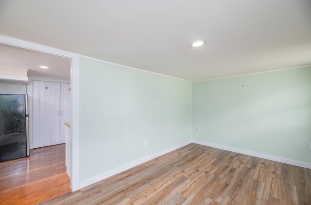 spare room featuring crown molding, light wood finished floors, and baseboards