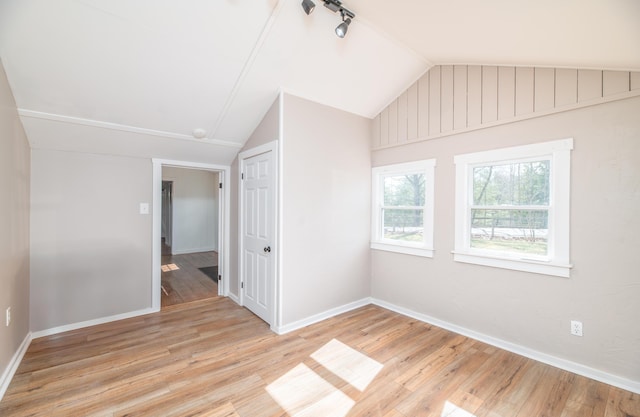 empty room featuring baseboards, vaulted ceiling, and light wood-style floors