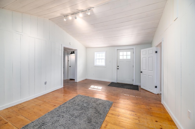 entrance foyer with baseboards, rail lighting, lofted ceiling, and light wood-type flooring