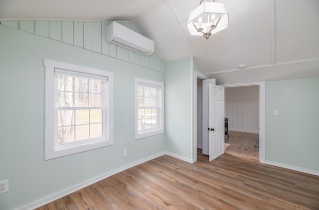 unfurnished room with baseboards, a wall unit AC, wood finished floors, and vaulted ceiling
