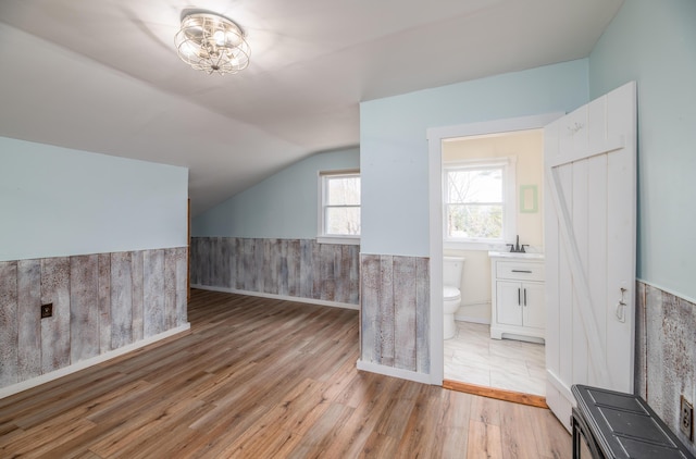 additional living space with a wainscoted wall, light wood finished floors, vaulted ceiling, and a sink