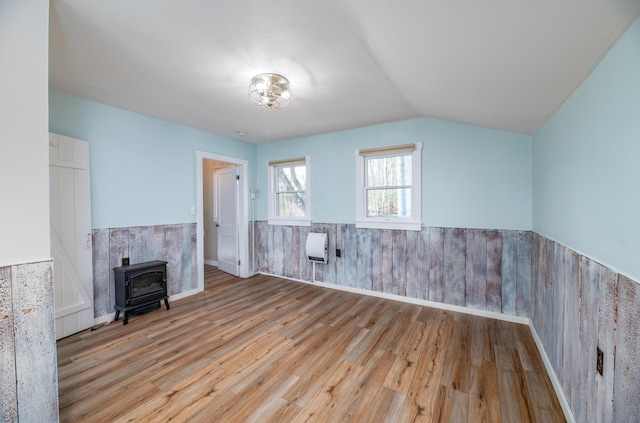 unfurnished living room featuring wainscoting, wood finished floors, a wood stove, and lofted ceiling